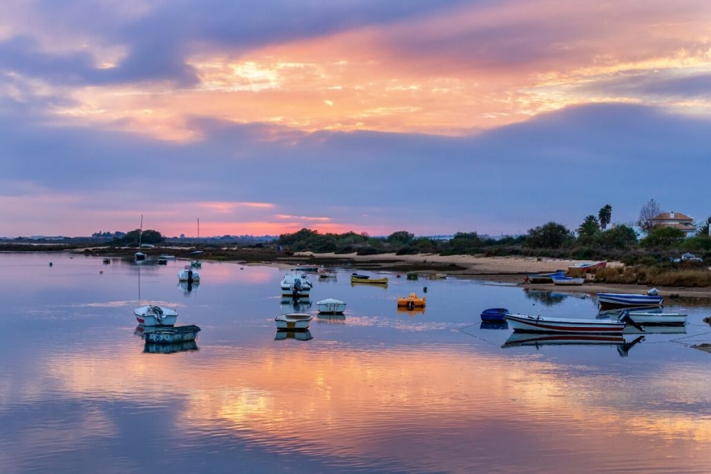 A picture of a purple sunset sky over the calm waters of Cabanas de Tavira with boats on the water