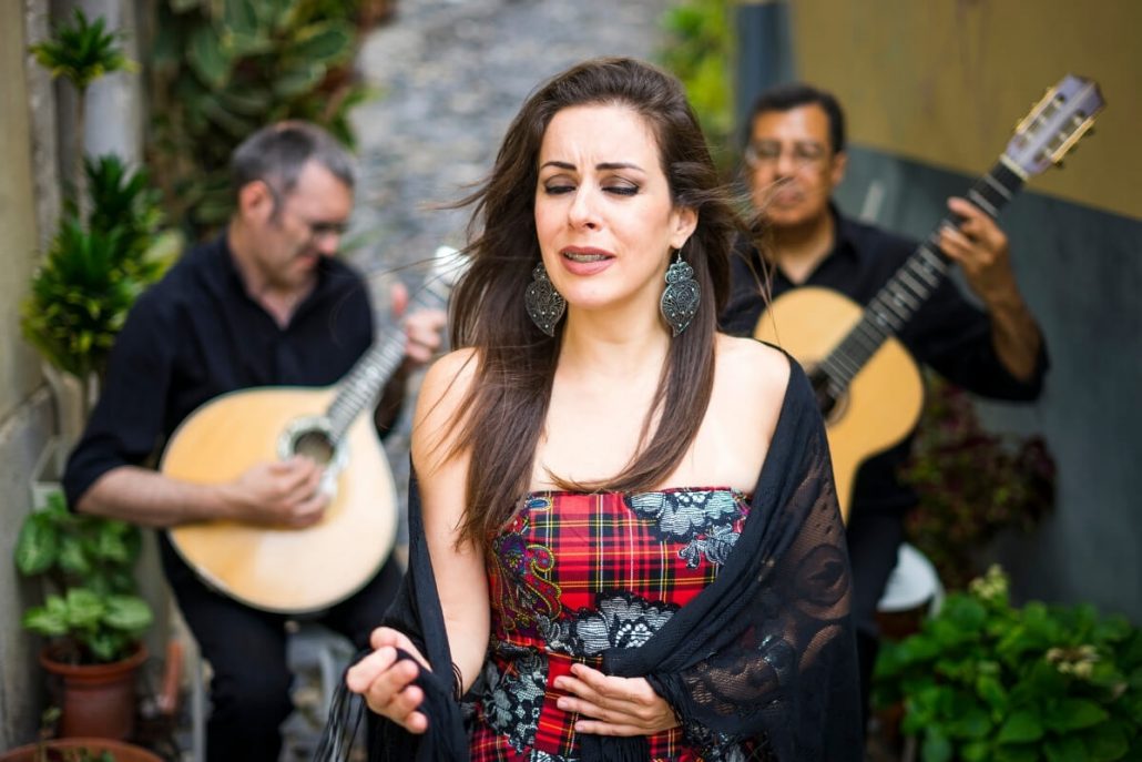 A picture of a Portuguese fado singer with two accompanying guitar players in the background